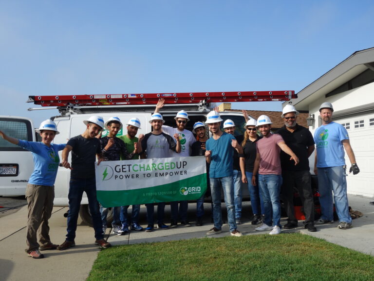 Team of workers in hard hats holding GetChargedUp banner in front of white service van with solar panel on roof