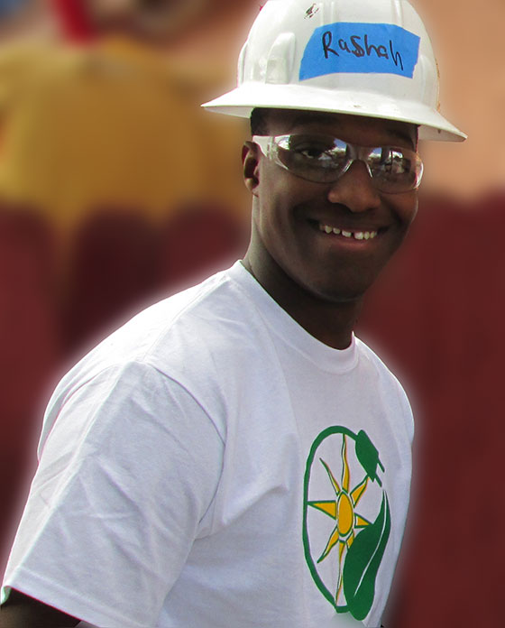 Man wearing hard hat with "Rashali" label and solar panel logo shirt, smiling at camera