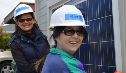 Two women in hard hats and safety gear stand beside a solar panel installation