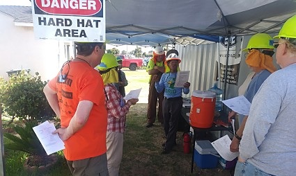 Construction safety briefing under hard hat area tent with workers in safety gear