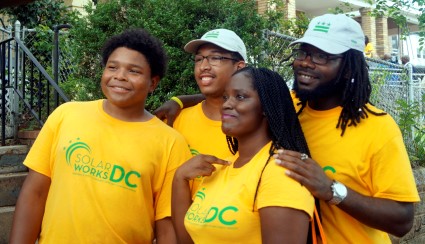 Four volunteers in yellow Solar Works DC shirts smile together outdoors