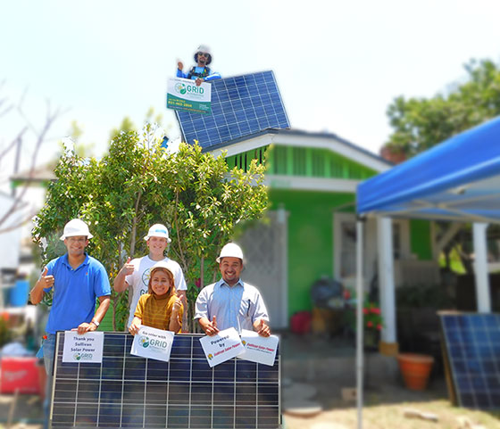 Group holding solar panels in front of green house with rooftop solar installation
