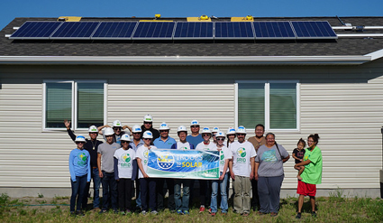 Group of people holding a "Solar Homecoming" banner in front of a house with rooftop solar panels installed