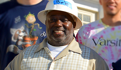 Man wearing white hard hat and light-colored jacket smiling at camera outdoors