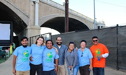 Seven people wearing GRID t-shirts stand together under a bridge at an outdoor event