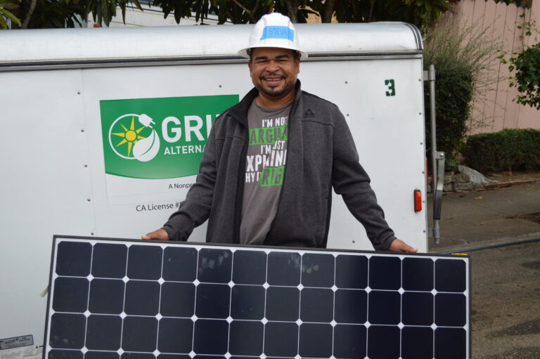 Smiling technician holding solar panel in front of green energy company van with California license displayed