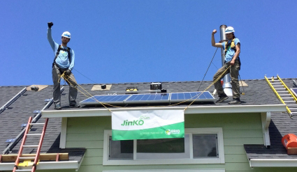 Two workers on roof installing solar panels on green building with Jinko sign