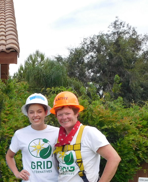 Two people wearing hard hats and GRID Alternatives t-shirts smile at camera outdoors