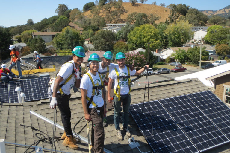 Four workers in hard hats and safety vests install solar panels on a residential rooftop in Novato