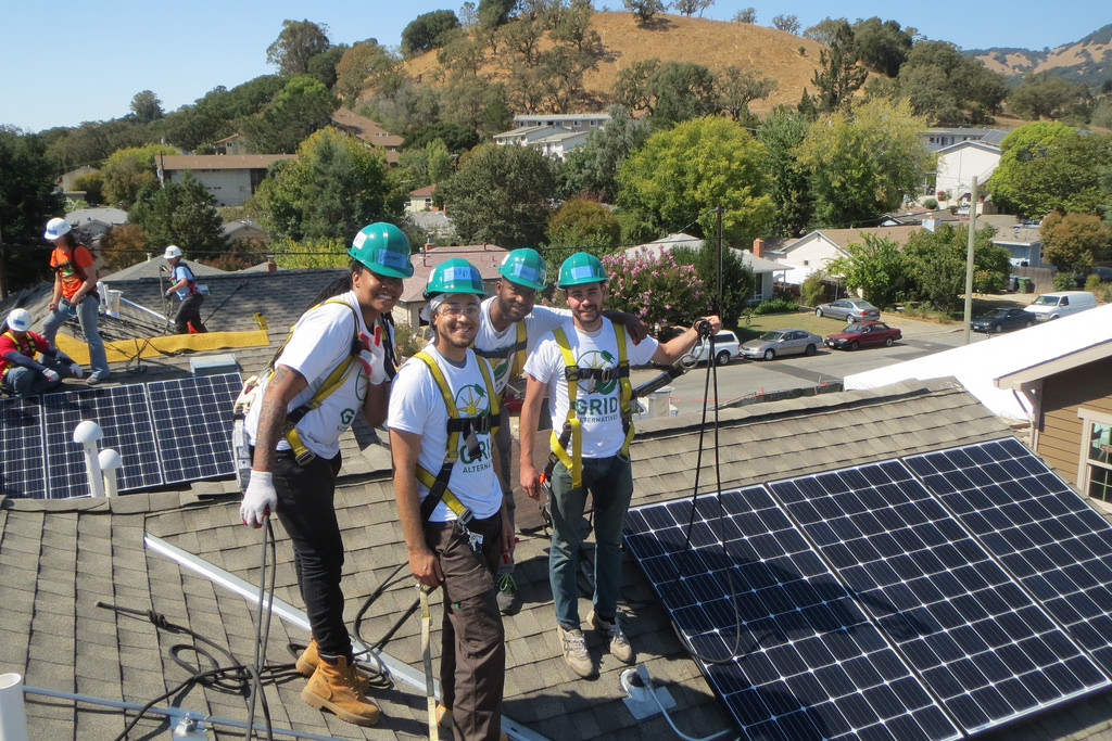 Four workers in hard hats and safety vests install solar panels on a residential rooftop in Novato