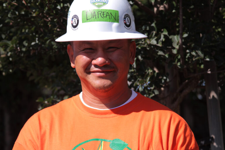 Man wearing white hard hat with "DAREAN" label and orange shirt, smiling outdoors