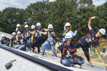 Group of women in hard hats and safety gear installing solar panels on a roof