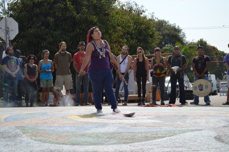 Woman dancing at community block party with spectators gathered around colorful ground designs