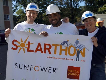 Three workers in hard hats hold a Solarthon banner with Sunpower and Wells Fargo logos at a solar installation event