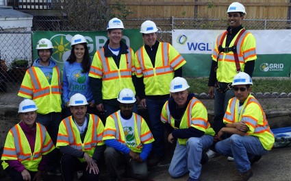 Construction crew of 12 workers in yellow safety vests and hard hats posing together at a job site