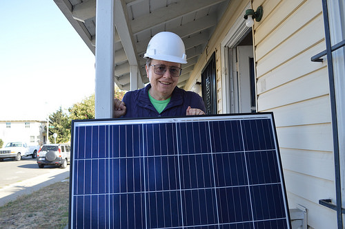 Worker in hard hat holding solar panel on residential porch