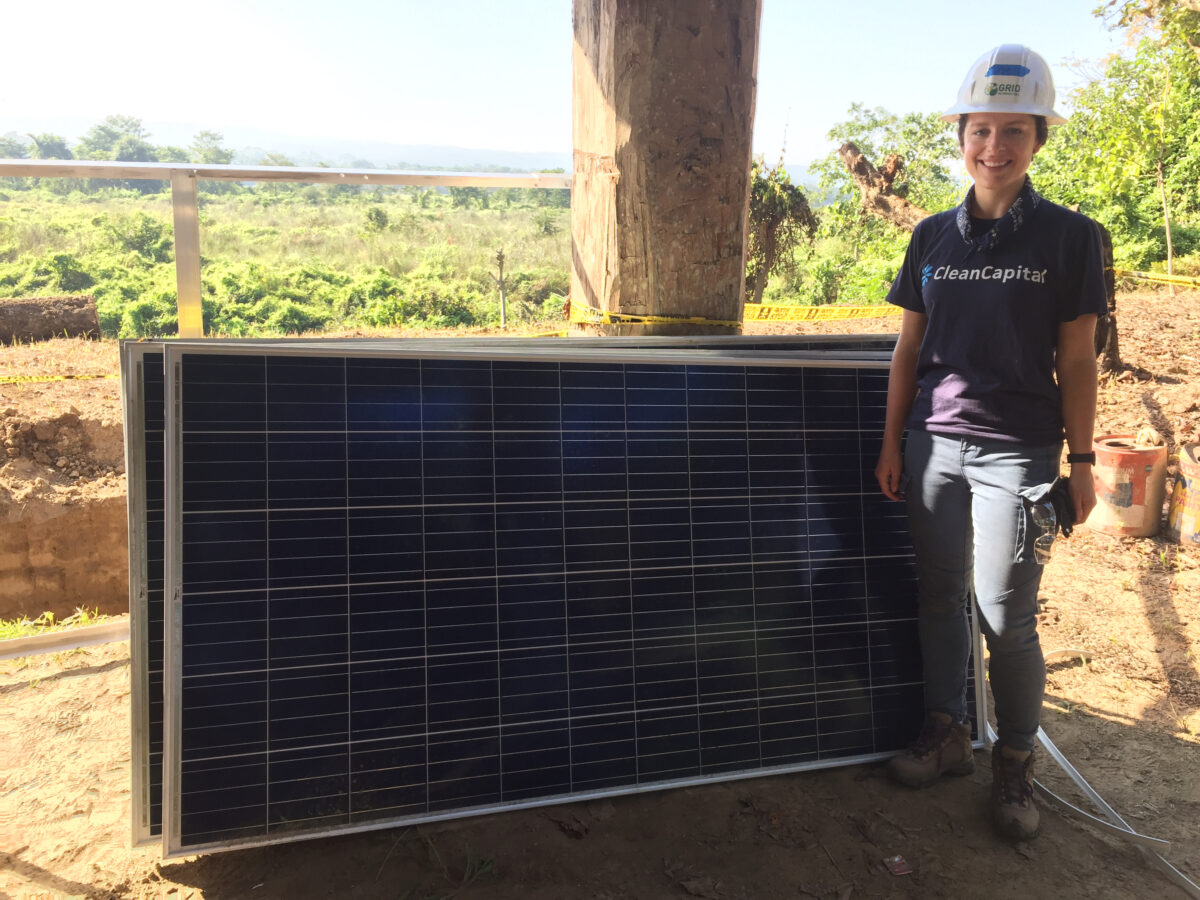 Woman in CleanCapital shirt holding solar panel at construction site overlooking green landscape