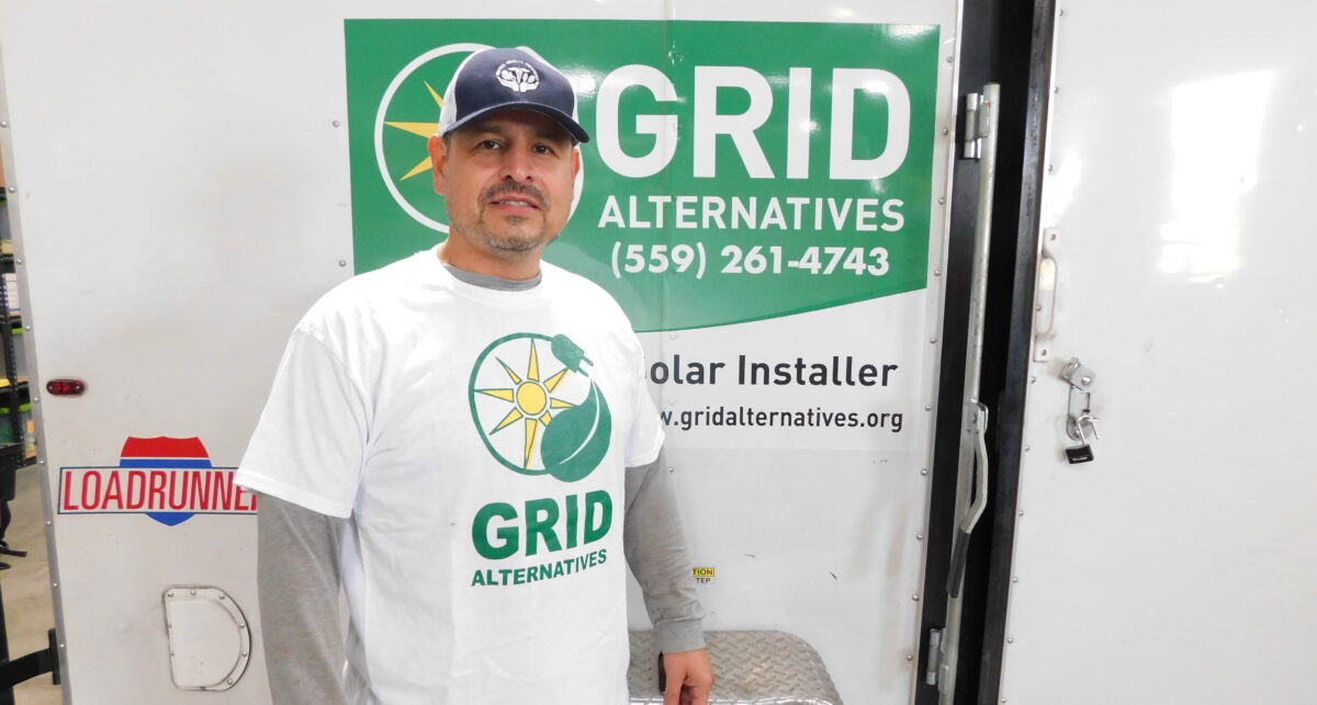 Man in Grid Alternatives solar installer uniform standing in front of branded van door with company logo and phone number (559) 261-4743