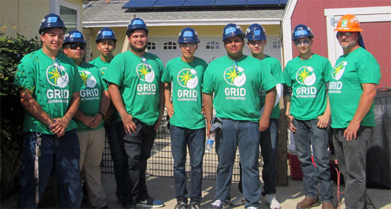Team of workers in matching green GRID shirts and hard hats posing together outdoors