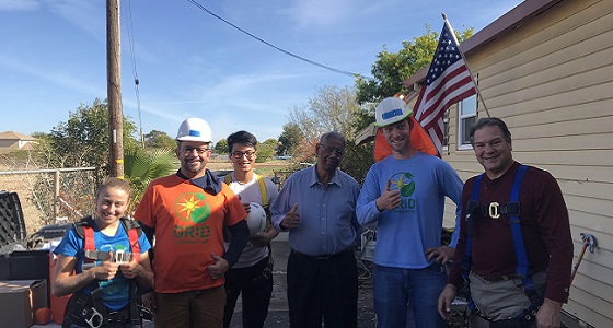 Group of people posing together outside a house with American flag during Veterans Day solar installation event