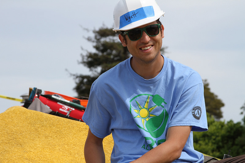 Wyatt Atkinson smiling at construction site wearing hard hat and blue shirt with sun logo