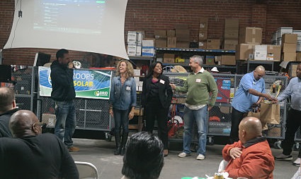 Group of people gathered indoors for volunteer and trainee appreciation event with solar panel display