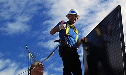 Worker in hard hat and safety gear installing solar panel on roof