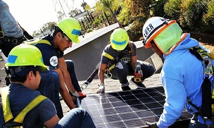 Workers in safety gear installing solar panels on a rooftop in Carson, 2017