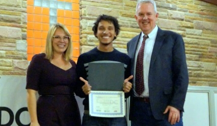 Three people smiling at a certificate presentation ceremony indoors