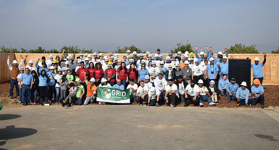 Large group of volunteers in colored shirts holding a GRiD banner at an outdoor solar energy event