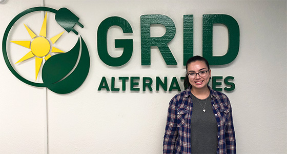 Person standing in front of Grid Alternatives logo with sun and leaf design
