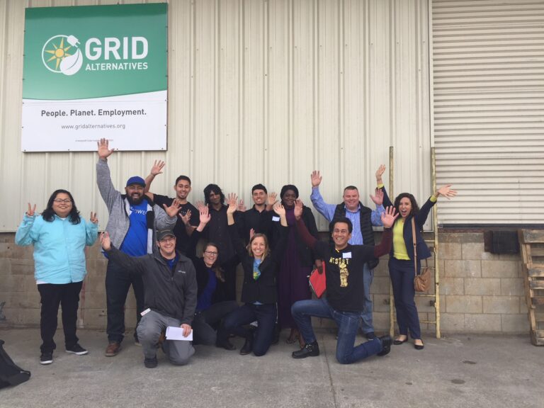 GRID Alternatives team celebrates in front of their building banner with "People. Planet. Employment." tagline