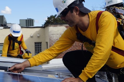 Two workers in yellow shirts installing solar panels on a rooftop