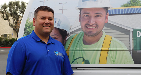 Man in blue polo shirt standing next to large billboard featuring construction worker in safety gear