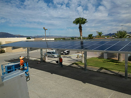 Solar panel carport with vehicles parked underneath and worker in safety gear on site