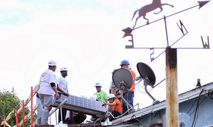 Construction workers installing solar panels on a rooftop with weather vane visible above