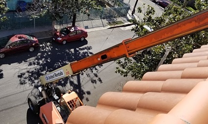 Aerial view of orange crane delivering solar panels to residential building in Los Angeles neighborhood