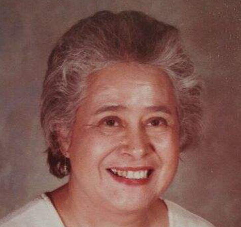 Portrait of a smiling older woman with gray hair wearing earrings against a brown background