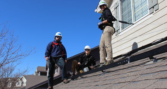 Three workers in hard hats on a residential roof during construction or repair work