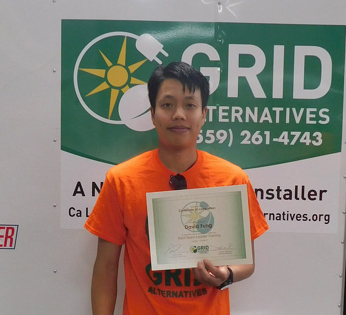 Person in orange shirt holding certificate in front of GRID Alternatives banner