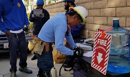 Construction worker in blue shirt and hard hat works with tools at outdoor training site, fire safety sign visible