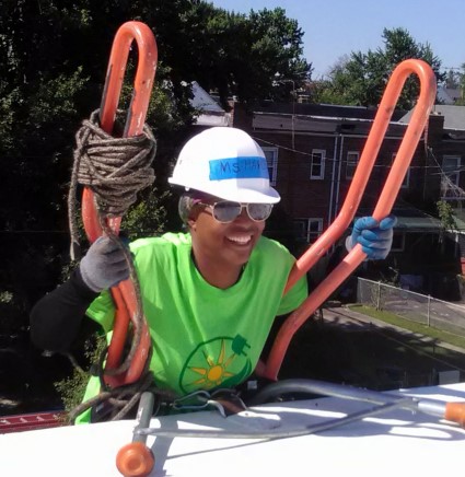 Homeowner Pamela wearing safety gear holds red rope while smiling on a roof