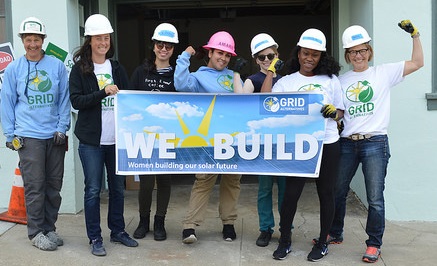 Team of volunteers in hard hats holding "We Build" banner at construction site