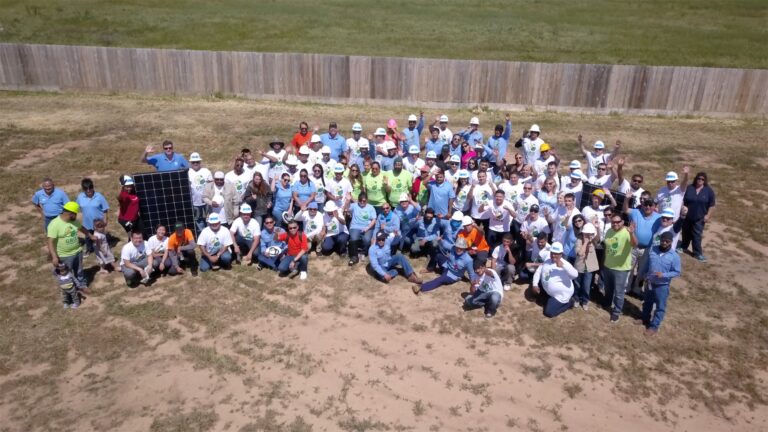 Large group of people wearing white hard hats gathered outdoors holding a solar panel, Central Valley's 2018 Solarthon event
