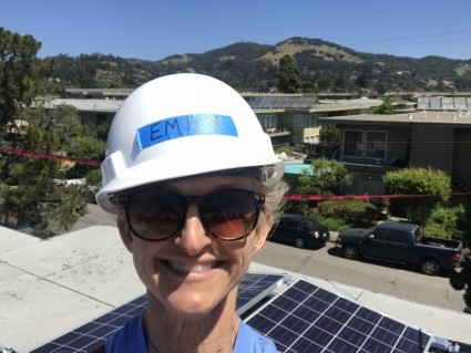 Woman wearing CEMI hard hat and sunglasses on rooftop with solar panels and hills in background