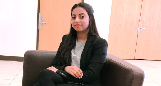 Woman in black blazer sitting on couch in office setting, looking at camera