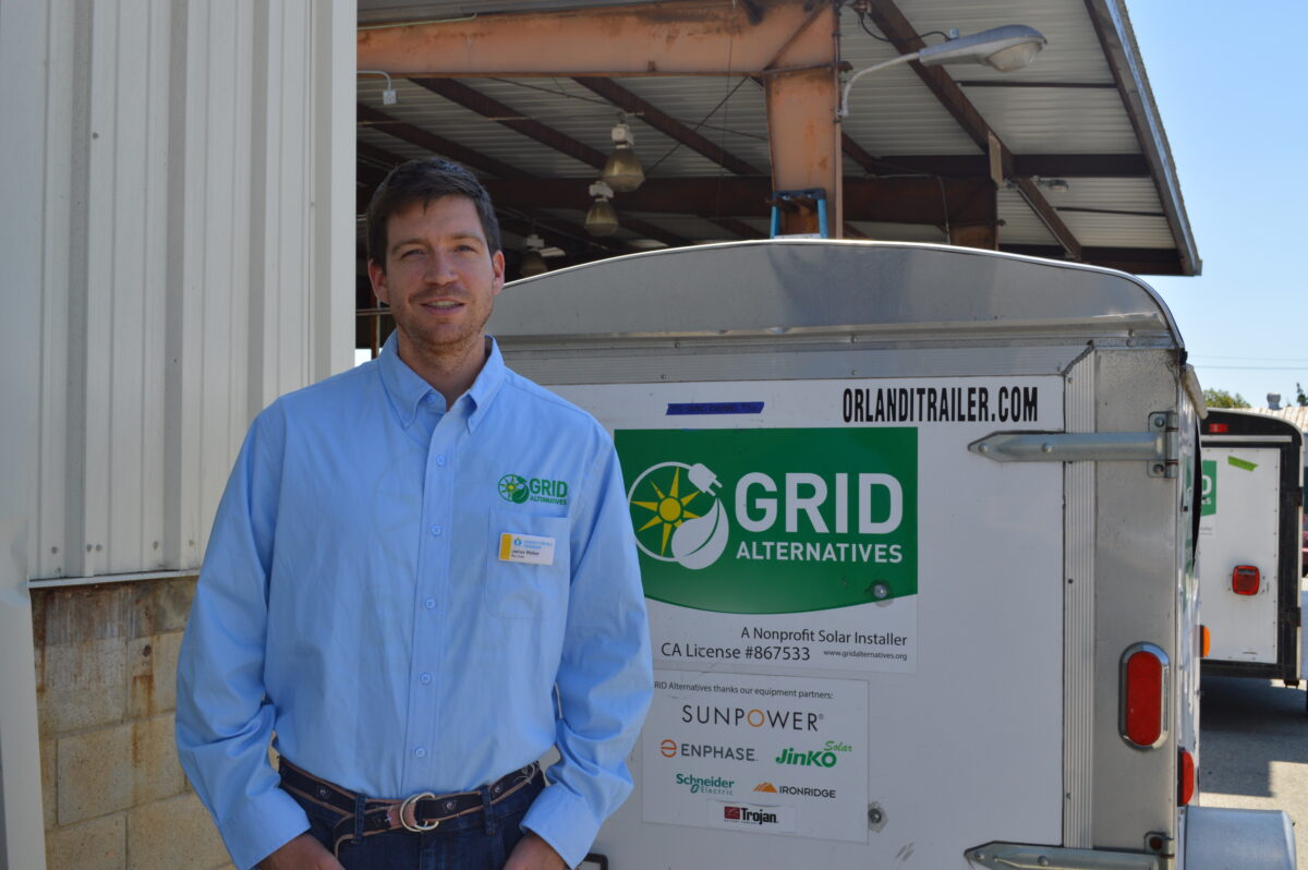 Man in blue shirt standing next to GRID Alternatives solar trailer at workshop facility