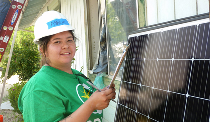 Worker in green shirt and white hard hat installing solar panel on rooftop