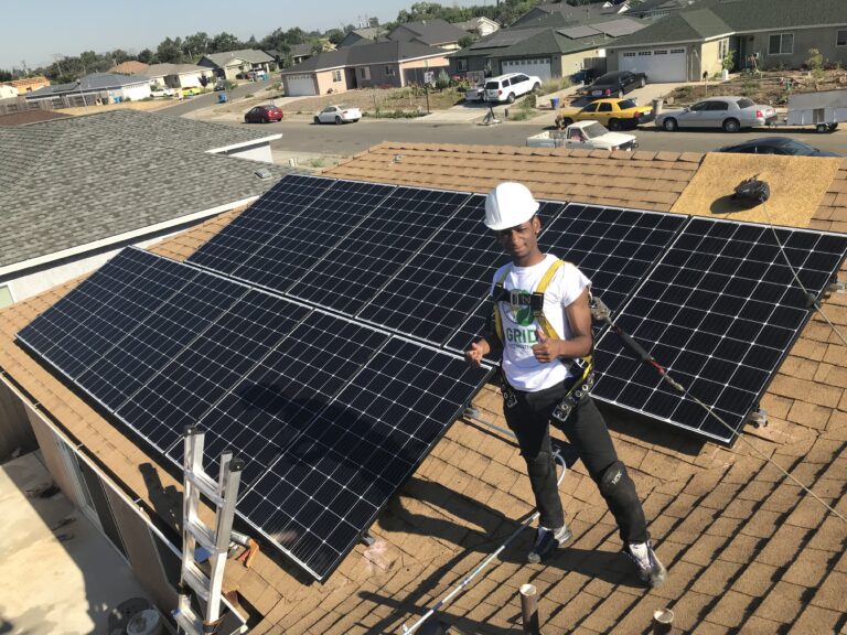 Solar installer in safety gear standing on residential roof with black solar panels during installation