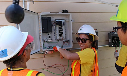 Four workers in safety gear installing a solar panel electrical system on a house exterior
